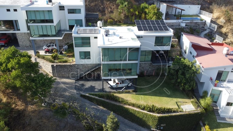 Aerial view of modern white residential house with solar panels, green roof, and curved landscaping in hillside neighborhood
