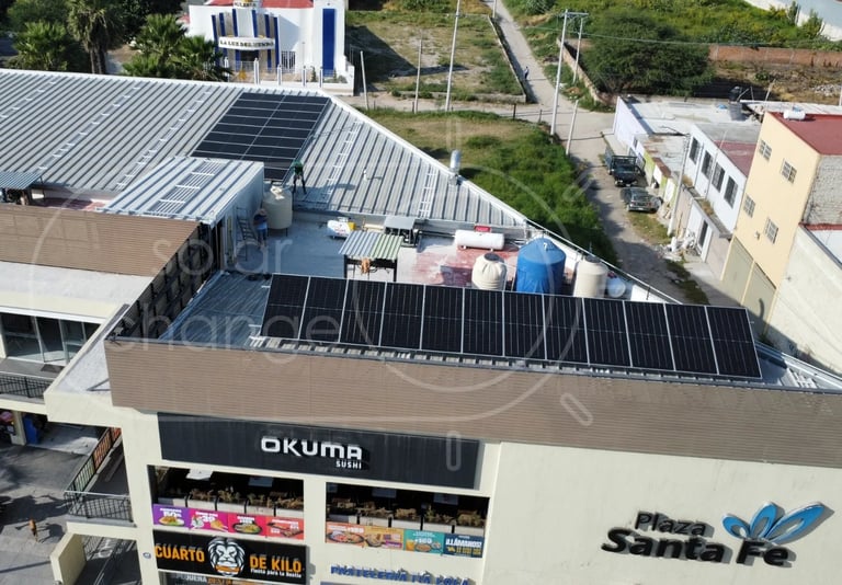 Aerial view of a commercial building with solar panels on rooftop and storefronts below, surrounded by residential homes and green hills