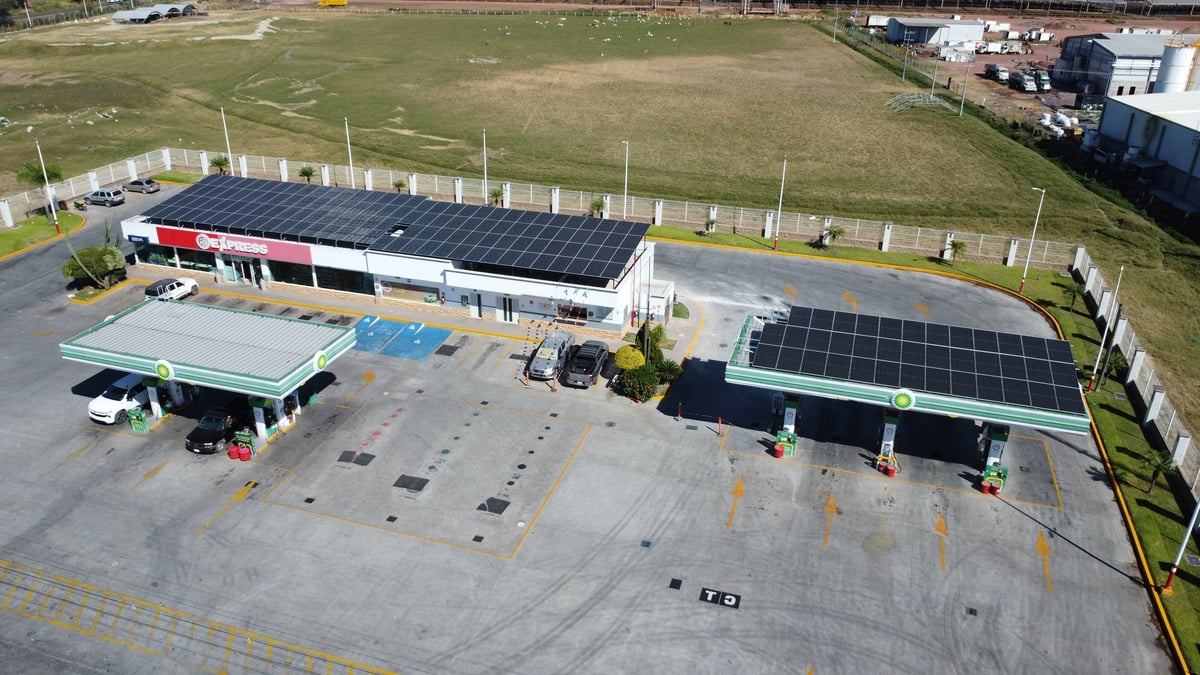 Aerial view of a commercial building with solar panels on the roof, parking lot, and surrounding green fields.