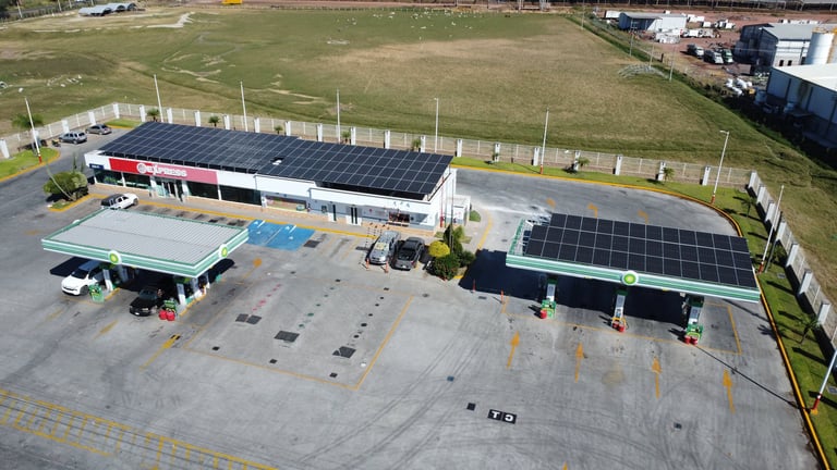 Aerial view of a commercial building with solar panels on the roof, parking lot, and surrounding green fields.