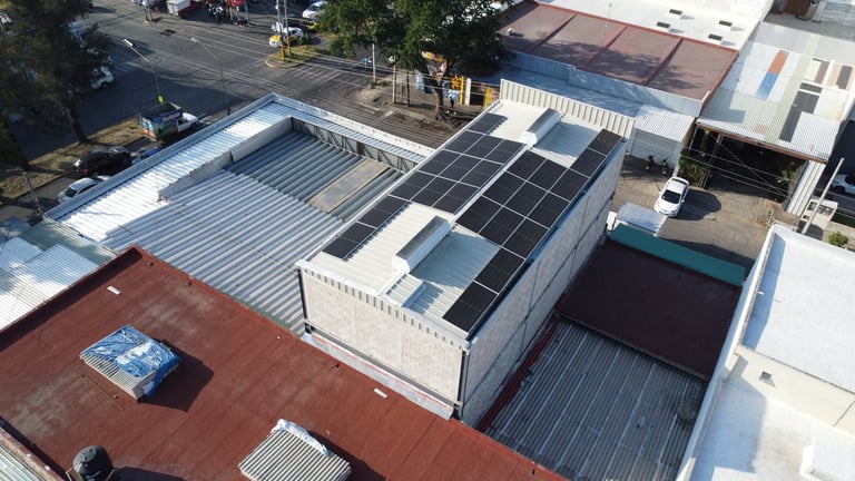 Vista aérea de una azotea comercial con paneles solares, contenedores metálicos y edificios contiguos